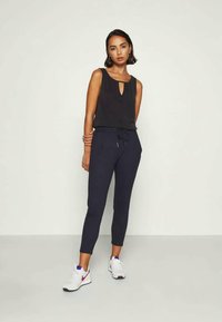 Black sleeveless top with keyhole cutout, paired with dark blue tapered pants and white sneakers with purple accents.