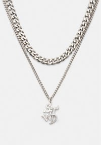 Silberne Halskette mit zwei Lagen, bestehend aus einer groben Kette und einer feinen Kette, die einen Anhänger mit der Aufschrift "ST WND" trägt. Strukturierte Metalloberfläche und modernes Design.