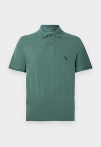 Polo-shirt en coton vert avec un col, deux boutons et un petit logo noir sur la poitrine. Manches courtes et ourlet droit.
