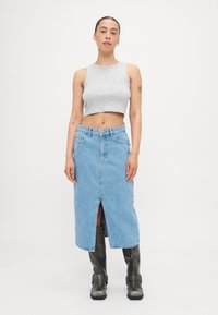 Pelēks īss tanka tops, kas apvienots ar gaiši zilu denim svārku ar priekšējo atvērumu. Modelis valkā melnas augstas zābakus ar sprādzēm.