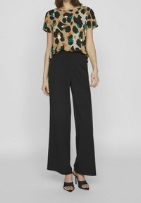 Top corto a maniche corte con stampa animalier in beige, marrone e teal, abbinato a pantaloni larghi neri. Modella con tacchi aperti neri.