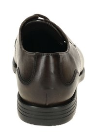 Bruine leren schoen met een afgeronde achterkant, gebogen stiksel details en een zwarte rubberen zool met horizontale groeven voor grip.