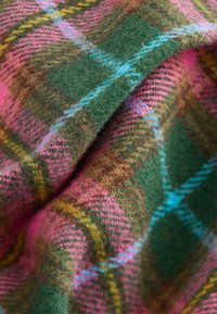 Wełniany koc z wzorem w tartan w kolorach zielonym, różowym, brązowym i niebieskim, o miękkiej teksturze i złożonym wzorze w kratkę.