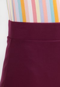 Cinturilla de tela burdeos de un vestido o falda, textura suave, combinada con una blusa de rayas multicolores que se ve parcialmente por encima.