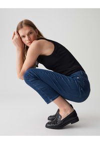 Débardeur noir côtelé, jean cropped bleu avec un léger stretch et mocassins en cuir noirs. Tenue simple et décontractée dans des tons neutres.