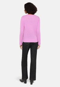 Pull en tricot rose à manches longues et col rond, associé à un jean noir à jambes droites et des bottines noires à talons.