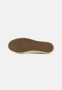 Brown rubber outsole with a textured surface, featuring a logo in the center. The edges are white, creating a contrasting border.