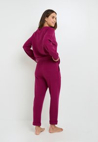 Ensemble de salon fuchsia comprenant un pull à manches longues et un pantalon à chevilles. Texture douce, coupe décontractée et poches latérales sur le pantalon.