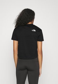 Svart kortärmad T-shirt med rund halsringning och texturerat mönster, med en vit logotyp på ryggen. Sammanställd med svarta åtsittande leggings.