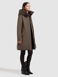 Smeđa podstavljena jakna s visokim ovratnikom, prednjim džepovima i zatvaranjem na patentni zatvarač. Nošena s crnim klinastim čizmama do koljena.