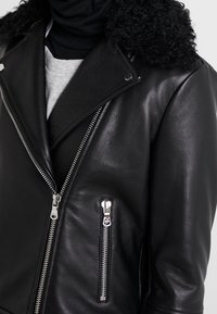 Giacca in pelle nera con un collo in morbida pelliccia nera testurizzata. Presenta una chiusura con zip asimmetrica e due tasche con zip.