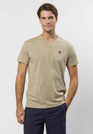 Beige v-hals t-shirt van gestructureerde stof, met een klein blauw logo op de linkerkant van de borst en korte mouwen. Draagt bij navy broek.