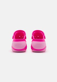 Rosa Crocs med en glatt yta, som har ett bakrem, ventilationshål och en texturerad sula. Varumärket "CROCS" är synligt på hälen.