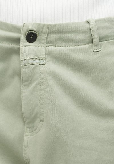 Ανοιχτό πράσινο παντελόνι με μαύρο κουμπί, φερμουάρ, θηλιές για ζώνη και διακριτική ραφή στην μπροστινή τσέπη, απεικονισμένο σε φόντο από λευκό ριγωτό ύφασμα.