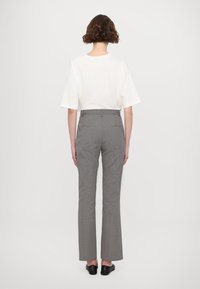 Haut blanc à manches courtes associé à un pantalon évasé noir et blanc à taille haute, présenté de dos. Chaussures noires à enfiler visibles.