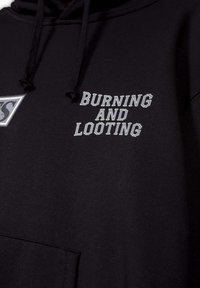 Sudadera negra de algodón con un bolsillo frontal. Presenta texto en blanco que dice "QUEMANDO Y SAQUEANDO", y un logotipo en la parte izquierda del pecho.