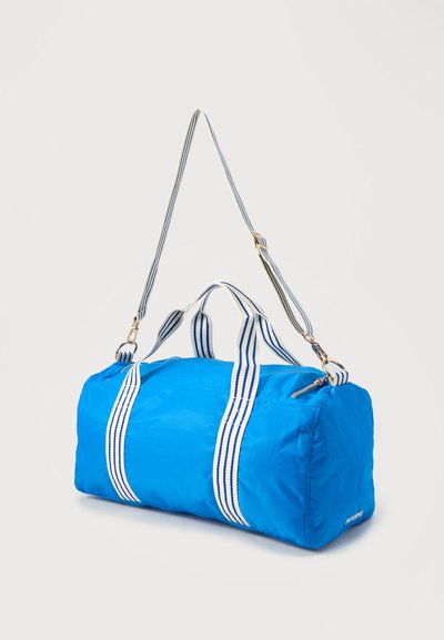 Μπλε σάκος duffel με λευκές και μπλε ριγέ λαβές και ρυθμιζόμενο ιμάντα ώμου, κλείσιμο με φερμουάρ στην κορυφή και απαλό ύφασμα.