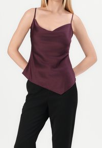 Haut asymétrique en satin prune avec des fines bretelles et un décolleté arrondi, associé à un pantalon noir ajusté. Texture lisse et tombé élégant.