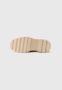 Semelle de chaussure en caoutchouc beige avec texture cannelée et motif segmenté, présentant un bout rond et un design de base plate.