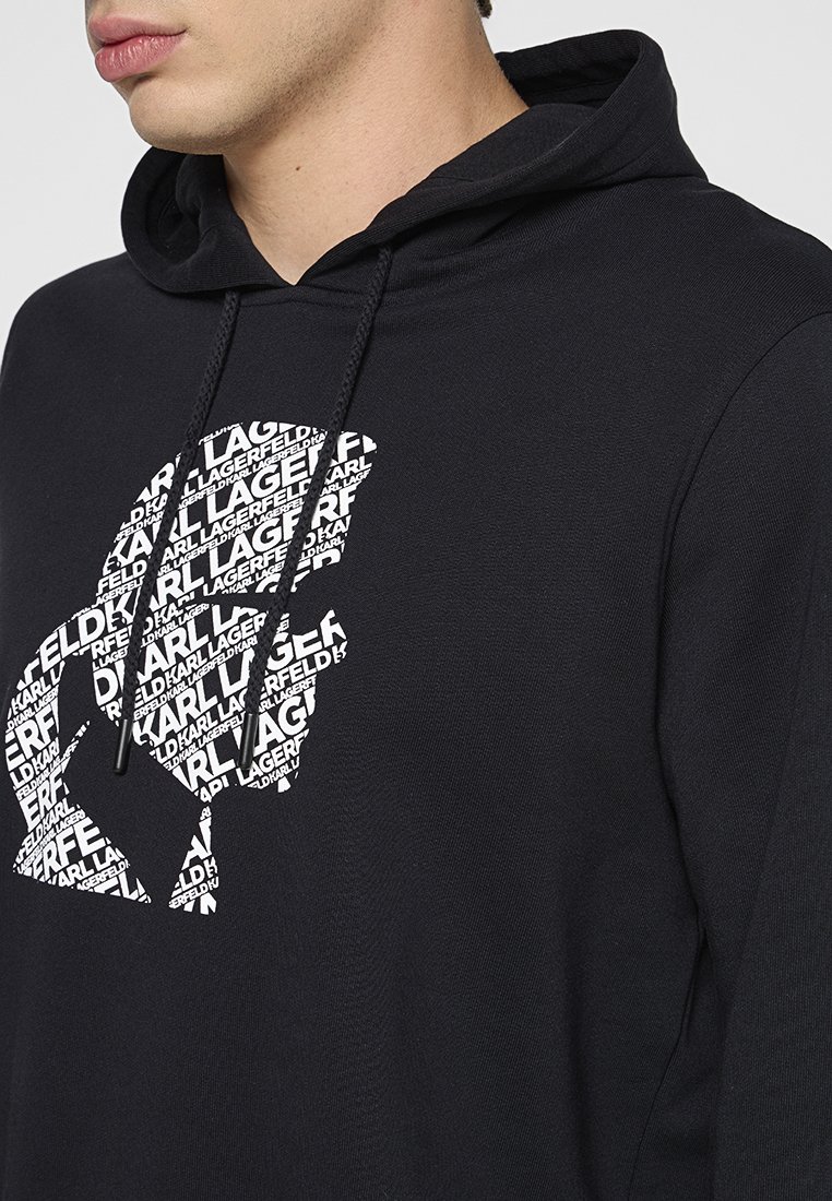 Haut à capuche noir en tissu doux avec un grand graphique de texte répété en blanc, affichant le nom de la marque dans différentes orientations.