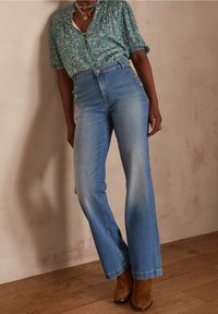 Camicia button-up floreale turchese abbinata a jeans azzurri a vita alta con bottoni laterali e design a gamba dritta. Stivaletti marroni alla caviglia.