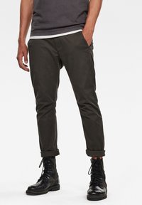 Ciemnozielone spodnie o zwężanym kroju, wykonane z lekkiej bawełny, z bocznymi kieszeniami i podwiniętymi mankietami, zestawione z czarnymi butami wojskowymi.