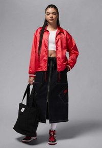 Punainen satiinitakki valkoisen crop topin päällä, yhdistetty pitkään mustaan farkkuhameeseen, jossa on taskut ja punaiset saumat, musta olkalaukku, punaiset lenkkarit.