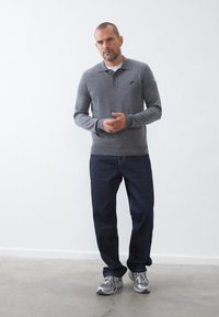 Grå langærmet polo med krave og tre knapper, parret med mørkeblå jeans og grå sportsko. Glat stof struktur.