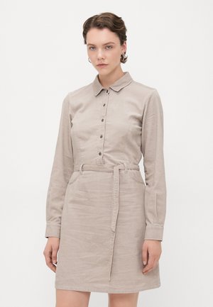 Beige kordfløyelskjole med kragegenser, knappelukking foran, lange ermer, belte i livet og to lommer. Teksturet stoff.