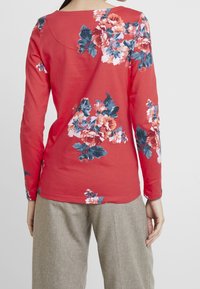 Pitkähihaisessa korallinvärisessä paidassa on pinkkejä, sinisiä ja vihreitä kukkakuvioita. Pehmeä kangas, venepääntie ja istuvat hihat.