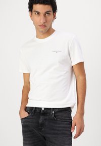 T-shirt bianca in cotone con scollo rotondo, maniche corte e un piccolo logo "TOMMY JEANS" stampato in colore scuro sul petto.