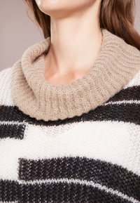 Maglione lavorato a maglia con un ampio collo alto beige, motivo a righe bianche e nere, e un corpo in maglia aperta e testurizzata.
