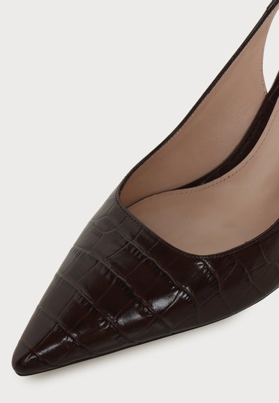 Gros plan d'une chaussure en cuir brun foncé à bout pointu avec une texture peau de crocodile et une doublure intérieure beige.