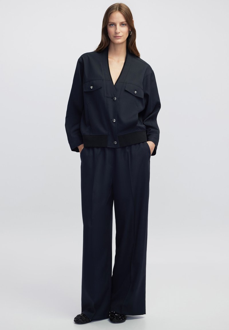 Chaqueta azul marino con dos bolsillos frontales y escote en forma de V, combinada con pantalones anchos azul marino. Ambos tienen una textura suave y un diseño minimalista.
