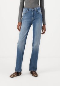 Jeans rectos de color azul claro con cintura alta, bolsillos delanteros y textura desgastada. Combinados con zapatos planos de estampado de leopardo.
