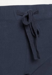 Ceinture à cordon de serrage bleu marine avec finition texturée et nœud. Présente des accents cousus sur le tissu. Détail pour tenue décontractée.