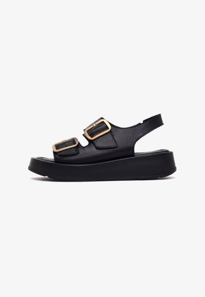 Black leather platform sandal with two gold buckle straps and back strap, rounded sole for added height and style.
