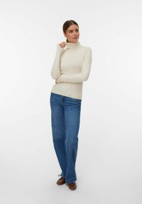 Suéter de cuello alto en crema combinado con jeans de pierna ancha azules. Textura suave, silueta ajustada y mangas largas con un detalle mínimo.