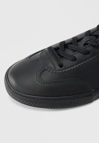 Μαύρο δερμάτινο αθλητικό παπούτσι με υφή στην επιφάνεια, στρογγυλεμένη μύτη και στρογγυλά κορδόνια. Διαθέτει επενδεδυμένο γιακά και ελαστικό πέλμα με σχέδιο.