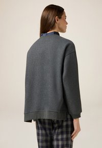 Grauer Sweatshirt mit lockerer Passform, strukturiertem Stoff und überschnittenen Schultern, mit einem dunkelblauen Kragen und kontrastierenden Saumdetails.