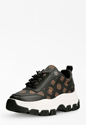 Zwarte sneaker met een bruin geometrisch patroon, dikke witte zool, zwarte profiel en zwarte veters op een witte achtergrond.