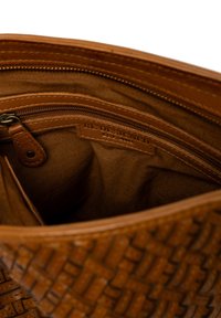 Interno di una borsa in pelle intrecciata marrone che mostra una tasca con zip e una fodera in tessuto con un'etichetta cucita che recita "RIDISEGNATO EST. 2013".