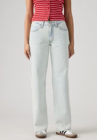 Φωτεινό μπλε τζιν με ίσια γραμμή, πέντε τσέπες και εμφανή ραφές. Συνδυασμένο με λευκά και γκρι αθλητικά παπούτσια.