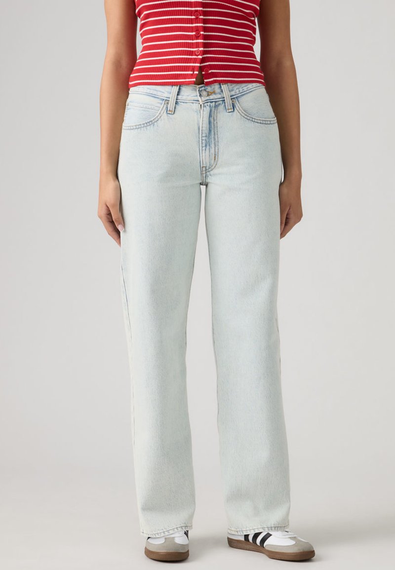 Φωτεινό μπλε τζιν με ίσια γραμμή, πέντε τσέπες και εμφανή ραφές. Συνδυασμένο με λευκά και γκρι αθλητικά παπούτσια.