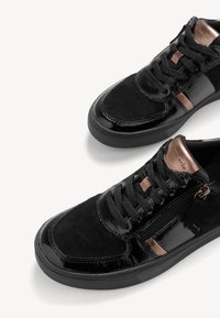 Black sneakers with a mix of shiny patent leather and suede. features bronze accents, round laces, and a side zipper for closure.
