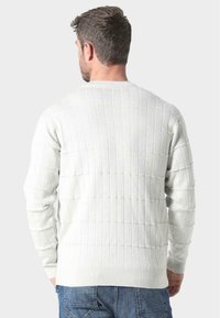 Biały sweter dzianinowy z teksturowanym wzorem siatki, okrągłym dekoltem i długimi rękawami, połączony z niebieskimi dżinsami na dole.