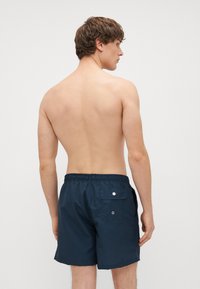 Tumes sinised ujumispüksid vertikaalsete triipudega, elastse vöökohtaga ja kahe tagakoti nuppudega sulgemisega.