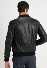 Zwarte leren jas met een getailleerd ontwerp, ribbelkraag en textuurpanelen. Heeft een gladde afwerking en elastische manchetten.