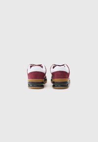 Maroon suede sneakers with white accents, featuring a brown rubber sole and black heel details. Smooth texture with contrasting colors.