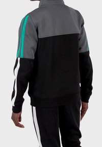 Svart och grå atletisk jacka med teal-accenter, hög krage, långa ärmar och vita sidostreck; mjuk textur, sportig design.